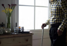 Tiny Habits That Quietly Boost Longevity Elderly man standing with a cane next to a table with flowers and medication