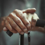 Close-up of elderly hands resting on a walking cane