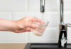 A hand holding a glass under a kitchen faucet as water is being poured into it
