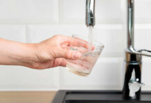 A hand holding a glass under a kitchen faucet as water is being poured into it