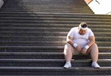 Hidden Training Hack for Rapid Muscle Growth An exhausted man in sportswear sitting on outdoor stairs, looking down.