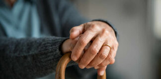 Close-up of elderly hands resting on a wooden cane