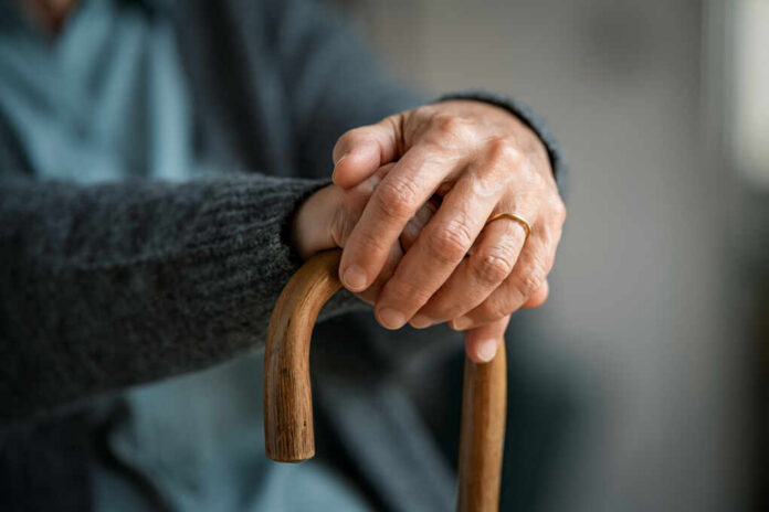 shutterstock_1889548966.jpg Close-up of elderly hands resting on a wooden cane