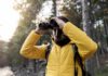 Person in a yellow jacket using binoculars in a forest