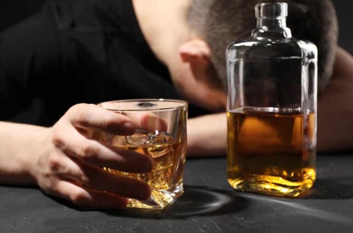 A person with their head down, holding a glass of whiskey next to a bottle