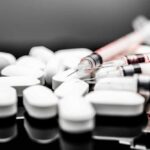 White pills and syringes arranged on a reflective surface