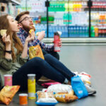 A young couple sitting on the floor of a grocery store enjoying snacks