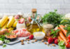 A variety of fresh foods including fruits, vegetables, and oils arranged on a table
