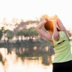 A woman stretching her arms by a lake during sunrise