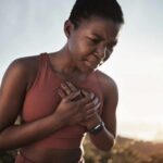 A woman in athletic wear holding her chest with a pained expression outdoors