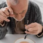 Elderly man focusing intently on a spoon while preparing to eat