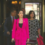 A group of women in professional attire exiting a building with security personnel