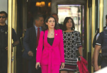 A group of women in professional attire exiting a building with security personnel