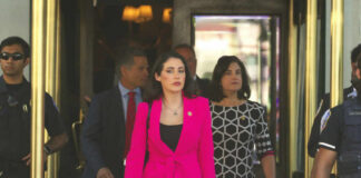 A group of women in professional attire exiting a building with security personnel