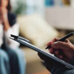 Brain Hack: How Words Rewrite Anxiety A therapist taking notes during a session with a client in the background