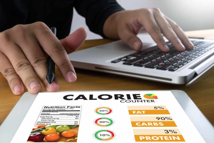Person using a calorie counter app on a tablet while working on a laptop