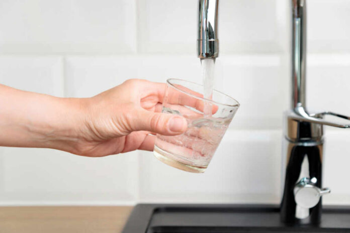 A hand holding a glass under a kitchen faucet as water is being poured into it