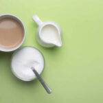 Coffee Timing Hack Boosts Longevity A cup of coffee, a bowl of sugar, and a creamer on a green background