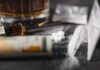 A close-up of a syringe, pills, and a glass of alcohol on a dark surface