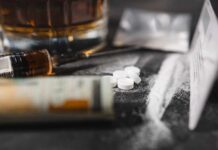 Meth’s SHOCKING Link To HIV A close-up of a syringe, pills, and a glass of alcohol on a dark surface