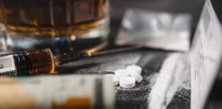 A close-up of a syringe, pills, and a glass of alcohol on a dark surface
