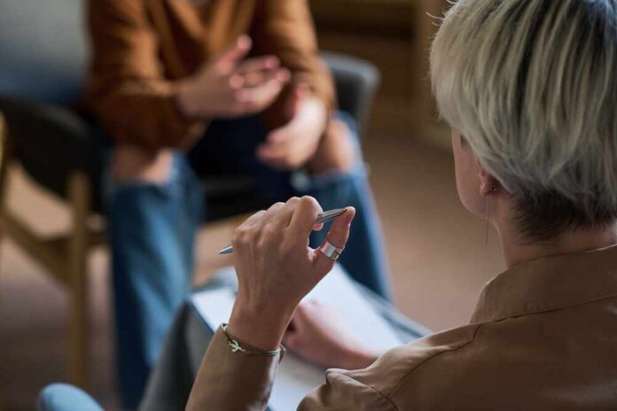 Adult,Woman,Holding,Pen,And,Taking,Notes,While,Listening,To Two individuals engaged in a conversation during a counseling session