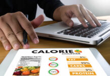Protein Bar Myths BUSTED – Watch Before Buying! Person using a calorie counter app on a tablet while working on a laptop
