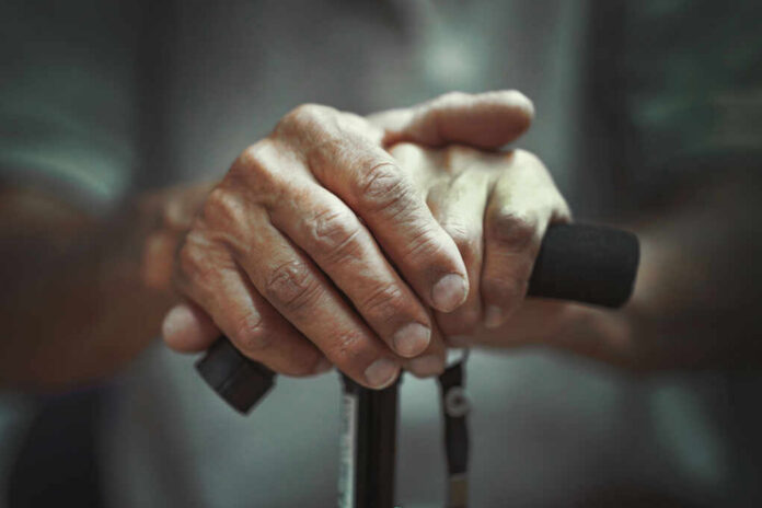 Close-up of elderly hands resting on a walking cane