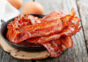 Bacon’s Quiet Threat: What Doctors Won’t Yell Crispy bacon strips in a cast iron skillet with eggs in the background