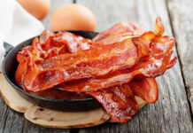 Bacon’s Quiet Threat: What Doctors Won’t Yell Crispy bacon strips in a cast iron skillet with eggs in the background