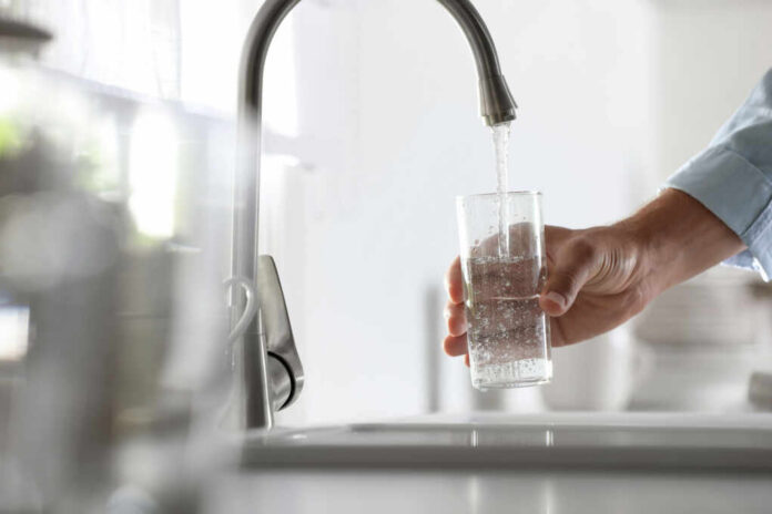 shutterstock_1928623259 A hand holding a glass under a kitchen faucet while water is being poured into it