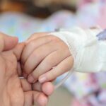 A childs hand with an IV drip being held by an adult hand