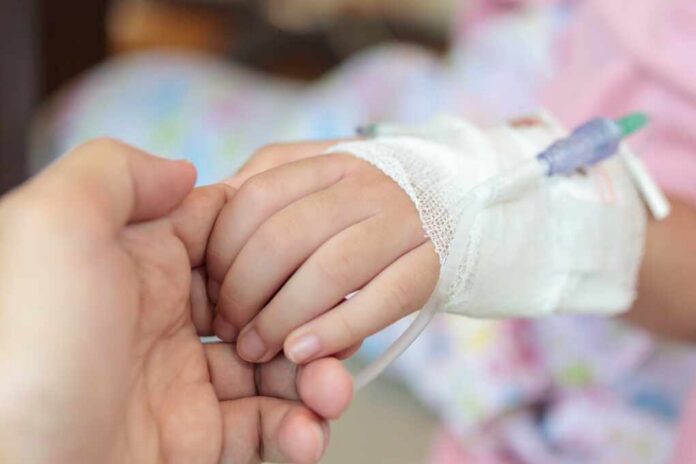 Mother,Holding,Child,Hand,With,Saline,Iv,Solution,In,Hospital A childs hand with an IV drip being held by an adult hand