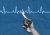 A hand holding scissors above a heartbeat line on a blue background