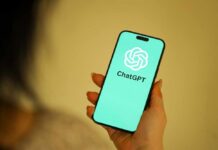 A person holding a smartphone displaying the ChatGPT logo on a teal background