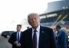 Trump’s Missing Drug Raises Transparency Firestorm A political figure in a suit looking thoughtfully at an outdoor event with a ship in the background