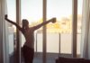 Woman stretching with coffee by a balcony window at sunrise