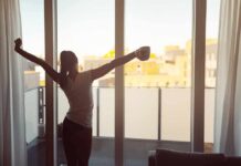 Woman stretching with coffee by a balcony window at sunrise