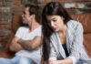 woman looking down while man sits with arms crossed on couch