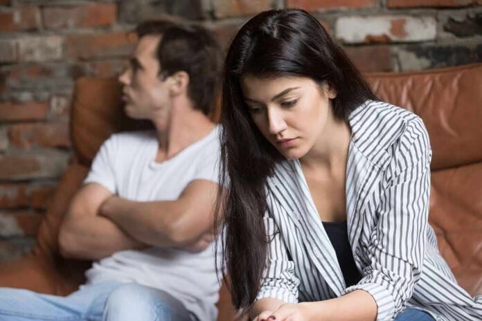 shutterstock_1034150995 woman looking down while man sits with arms crossed on couch