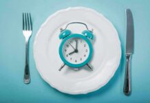 Eat Early, Outsmart? Rutgers Hints Yes Alarm clock on a white plate with fork and knife