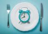Alarm clock on a white plate with fork and knife