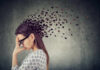 Microbe Plot Twist: Anxiety Isn’t In The Head A woman with glasses holding her head, with fragments dispersing from her head