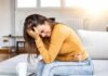 Stool STUCK in Rectum! Causes and Treatments Woman clutching her stomach in pain on a couch