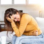 Woman clutching her stomach in pain on a couch