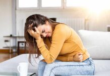 Stool STUCK in Rectum! Causes and Treatments Woman clutching her stomach in pain on a couch