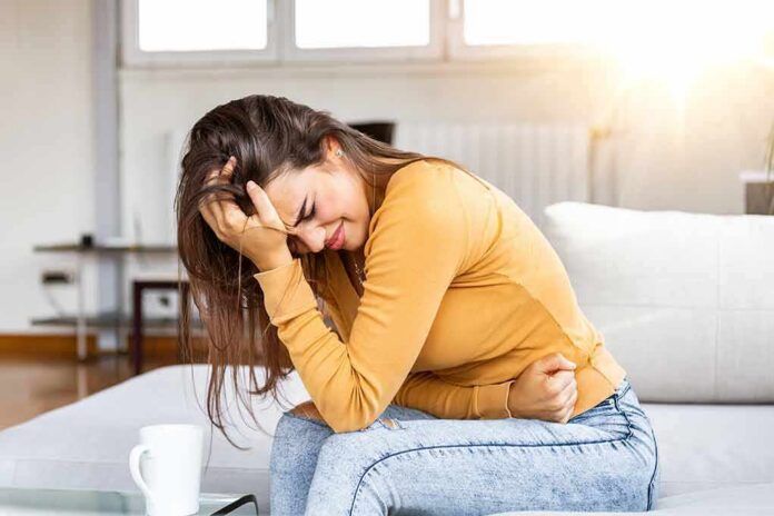 shutterstock_1682348995 Woman clutching her stomach in pain on a couch