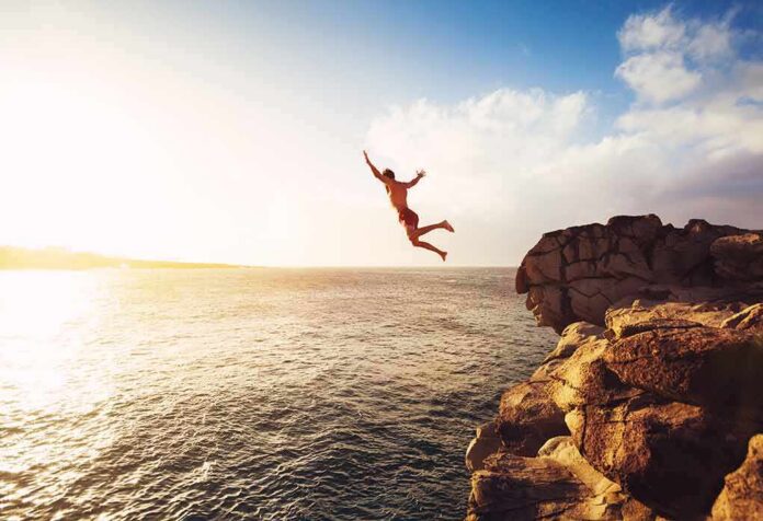 shutterstock_344995070 Person jumping off a rocky cliff into the ocean at sunset