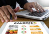 Government Protein Guideline Backfires On Seniors Person using a calorie counter app on a tablet while working on a laptop