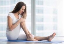 Woman sitting on yoga mat holding her lower leg in pain